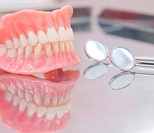 A full set of dentures designed for a person with missing teeth and dental instruments sitting on a table